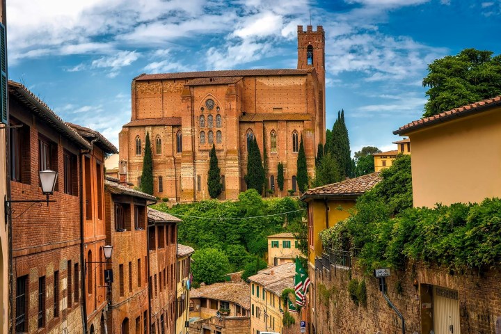 a group of people walking in front of a brick building with Basilica of San Domenico, Siena in the background