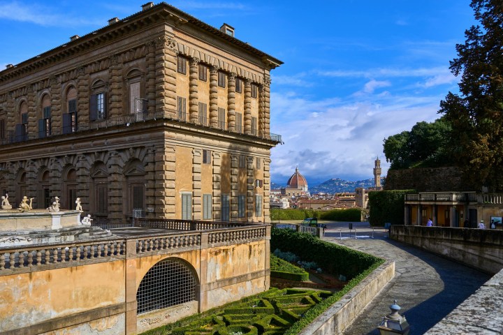 a large brick building with a clock tower with Palazzo Pitti in the background