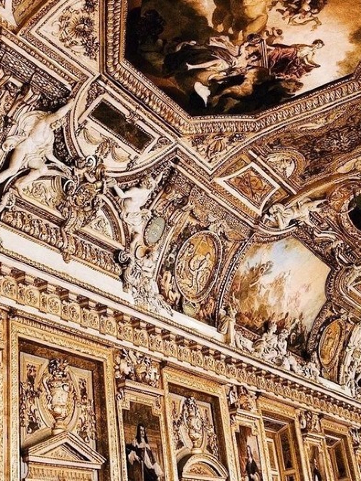 Ornate ceiling with paintings, sculptures, and gold embellishments in a grand hall.