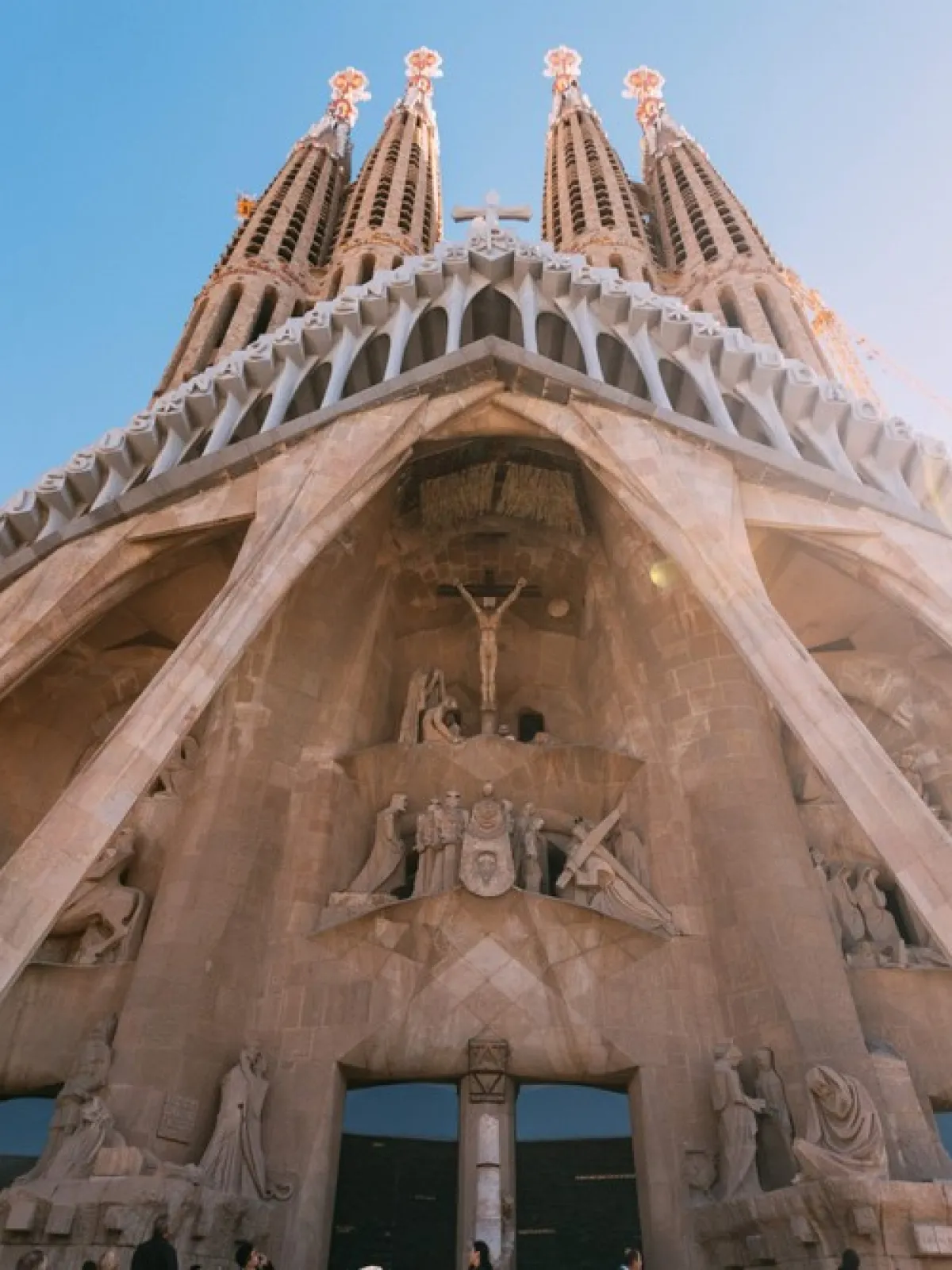 Upward view of a cathedral with intricate sculptures and tall spires against a clear sky.