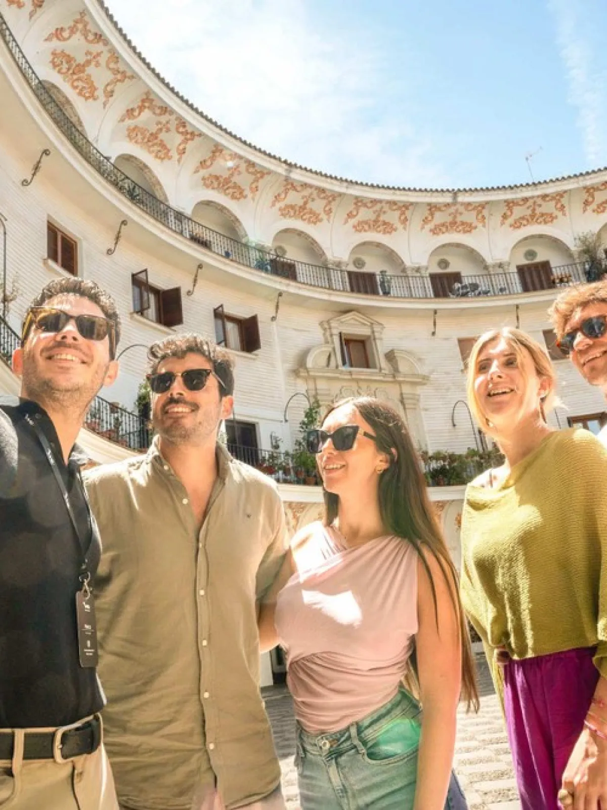 Five people taking a selfie inside a sunlit, ornate courtyard.