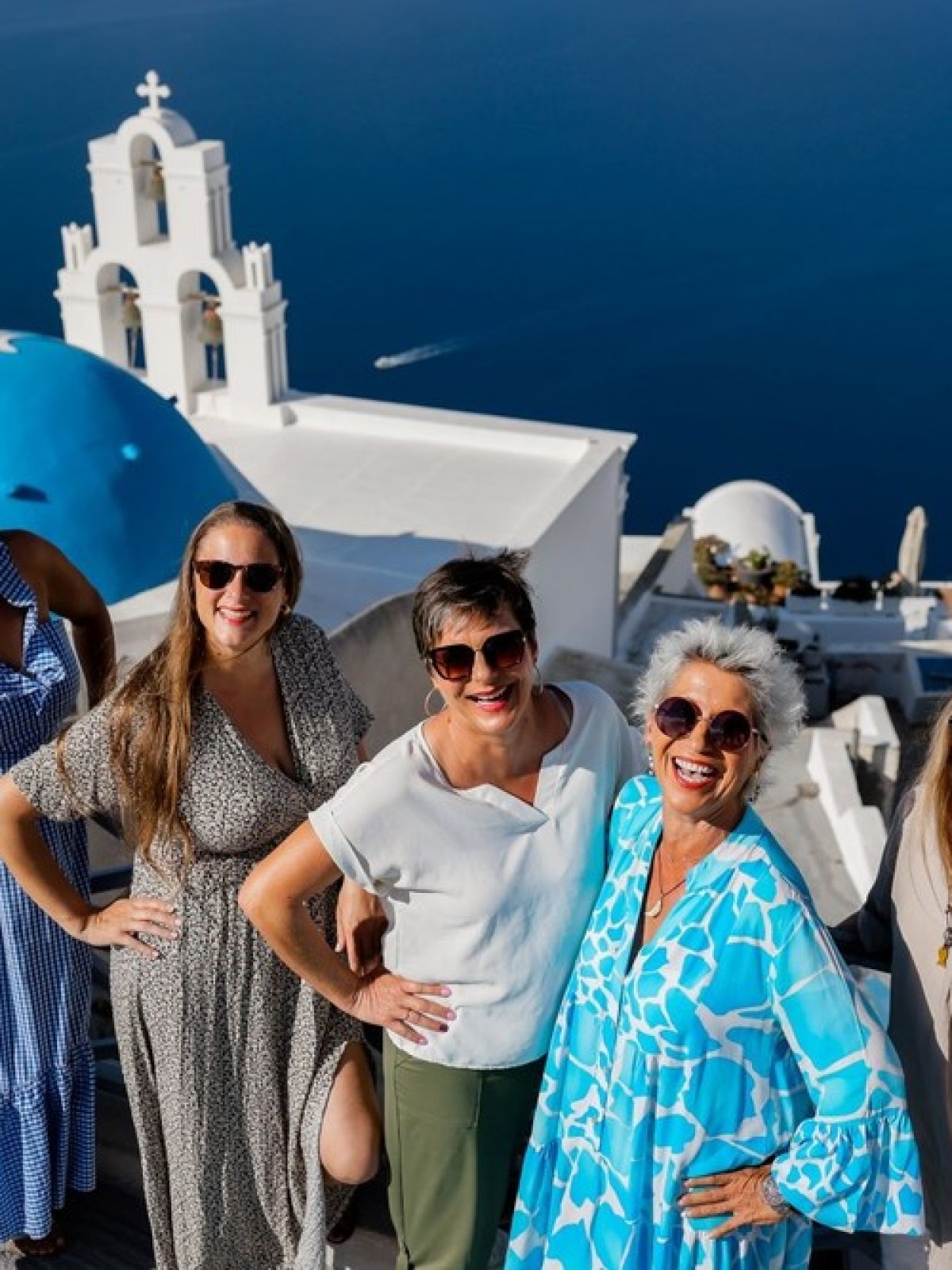 Five women smiling on stairs with a blue domed building and sea in the background.