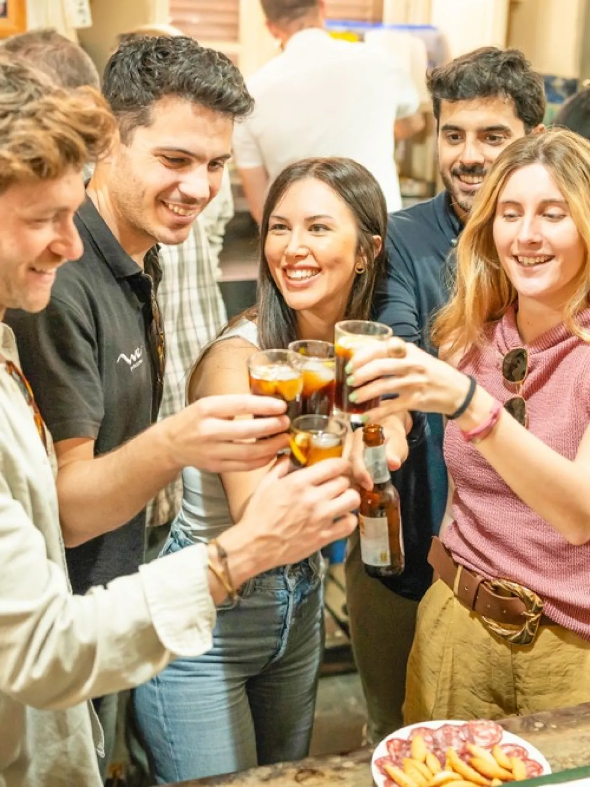 Group of people smiling and toasting with drinks in a lively indoor setting.