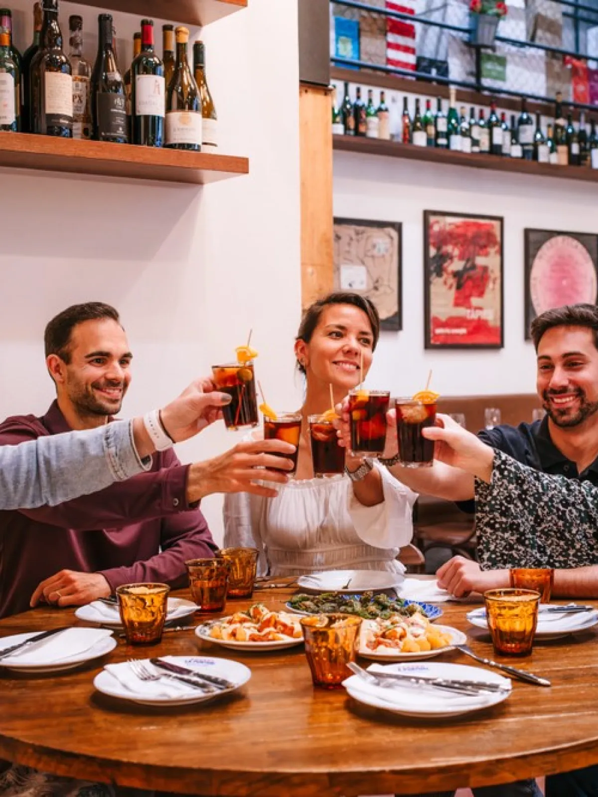 Group of five people toasting drinks around a table with plates and glasses in a cozy restaurant setting.
