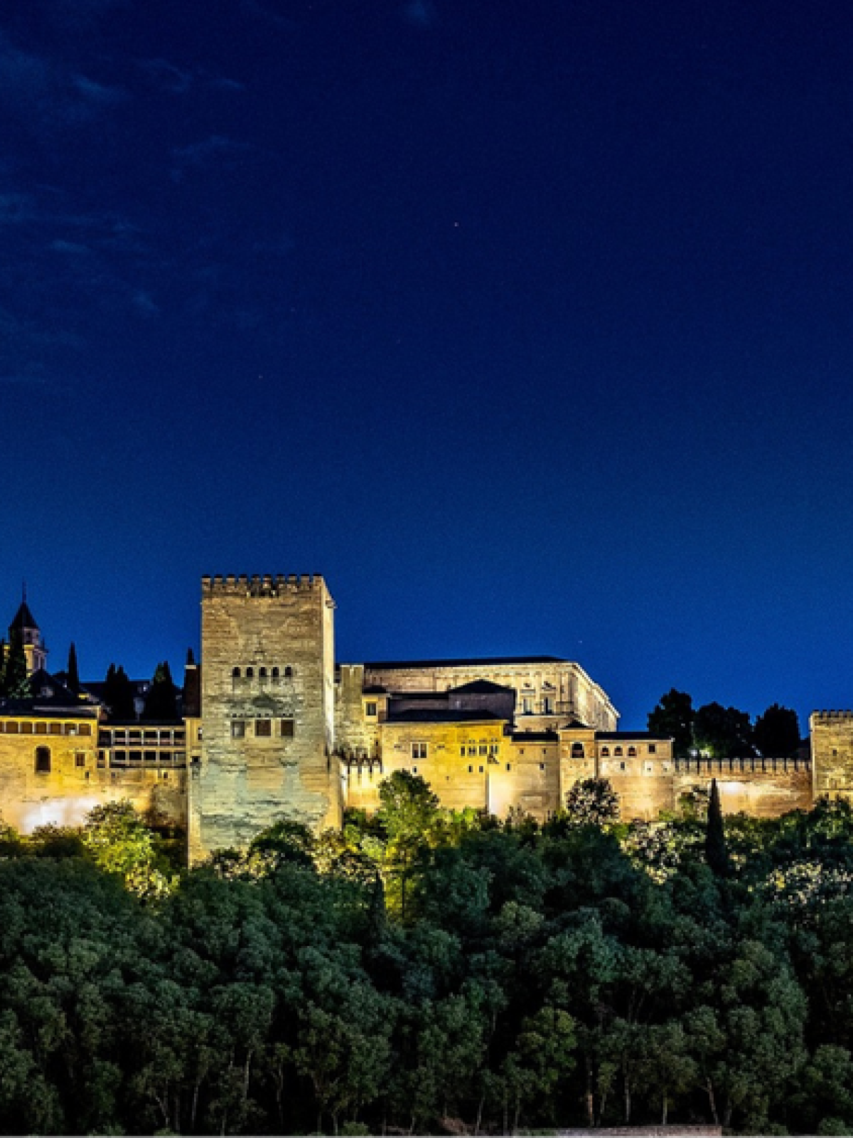 Illuminated historic fortress with towers at night against a dark blue sky.