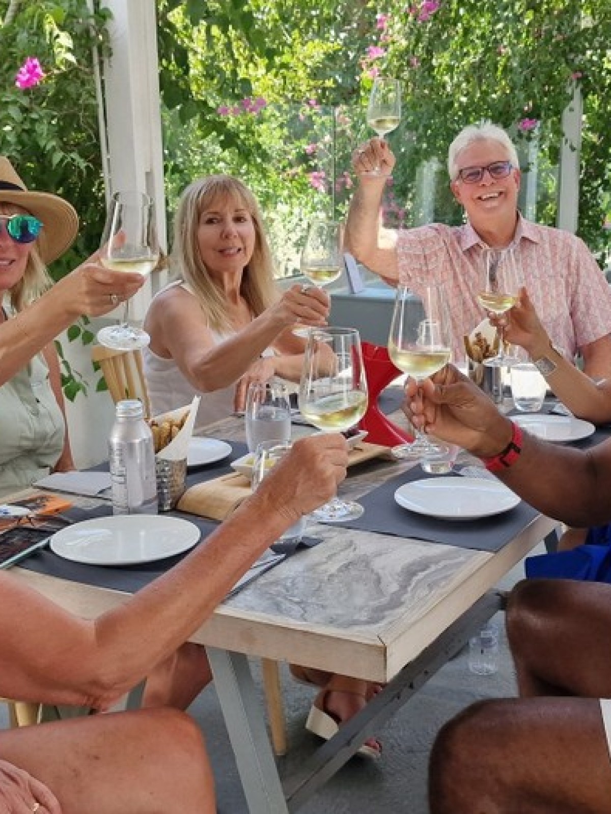 Group of six people at a restaurant table, smiling and toasting with wine glasses.