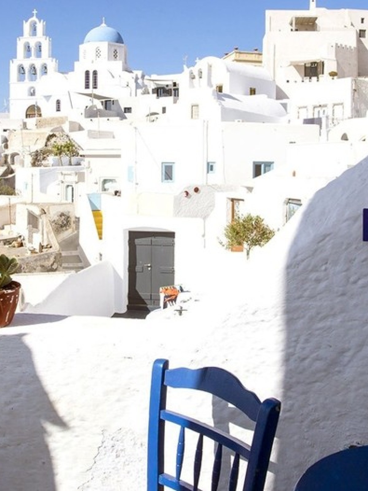 Santorini village view with white buildings, blue domes, and chairs on a terrace.