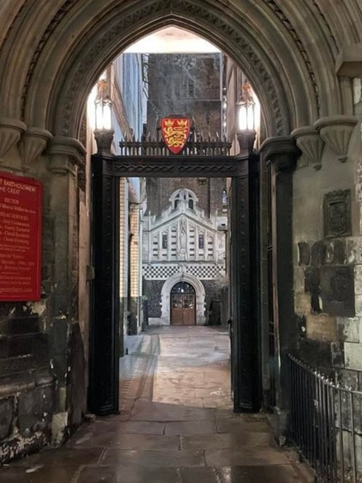 Archway leading to a courtyard with historical architecture and a crucifix on the right wall.