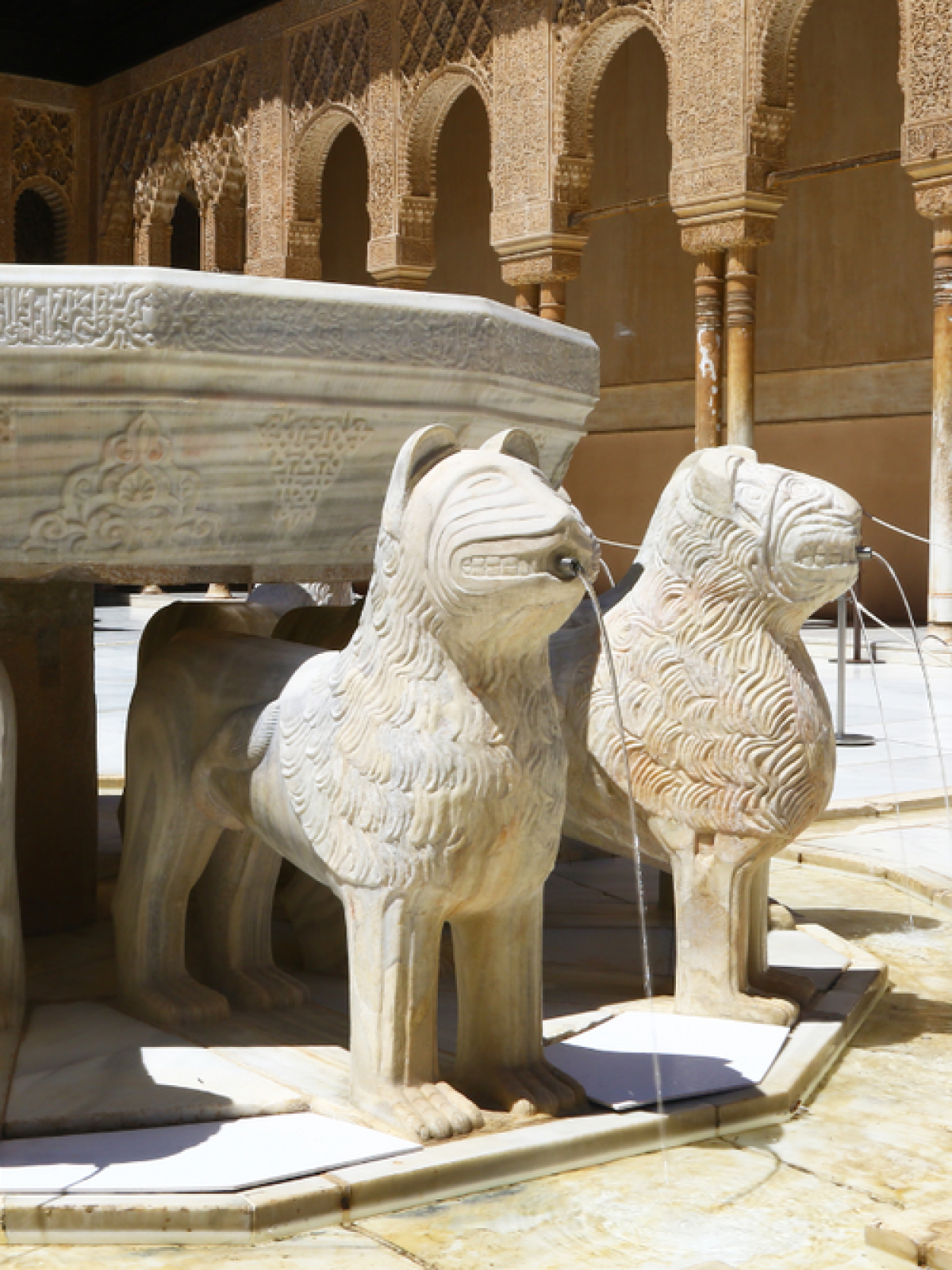 Ornate stone fountain with lion sculptures spouting water in a sunlit courtyard.