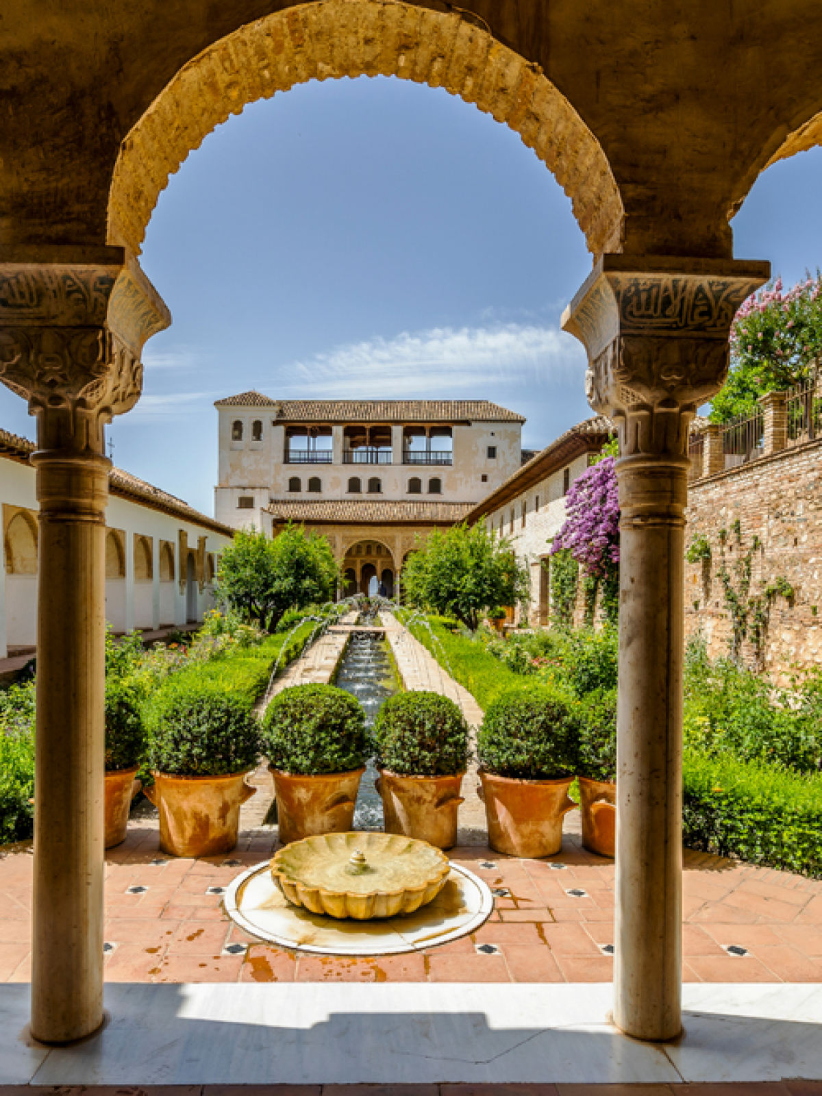 A historic garden with arches, a central fountain, and lush greenery on a sunny day.