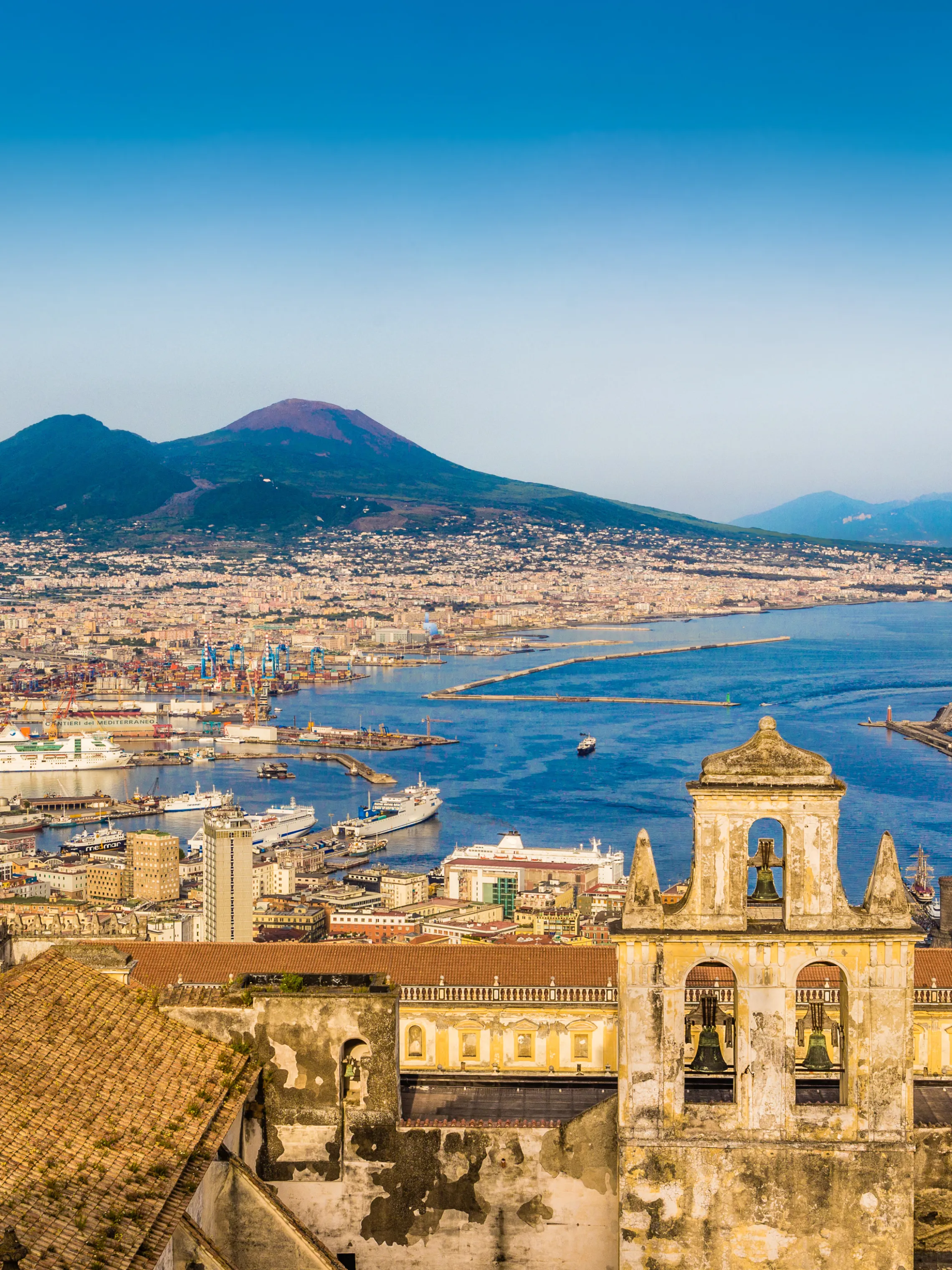 Aerial view of a coastal city with a volcano in the background under a clear blue sky.