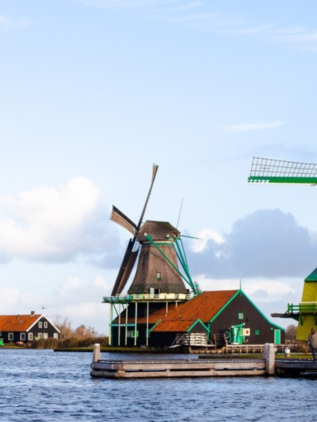 Three traditional Dutch windmills by a river under a partly cloudy sky.