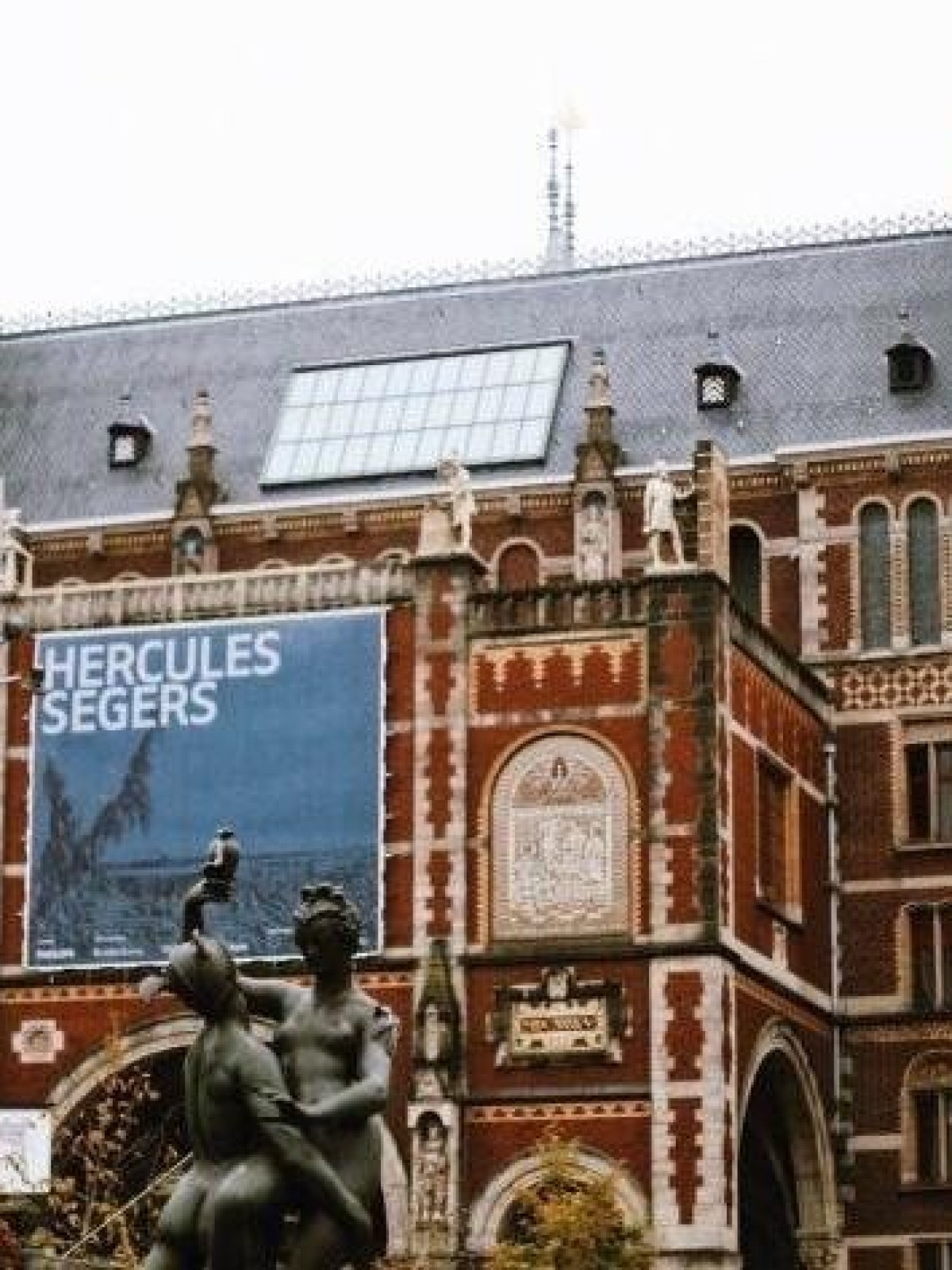 Historic brick building with statue in front and 'Hercules Segers' banner displayed.