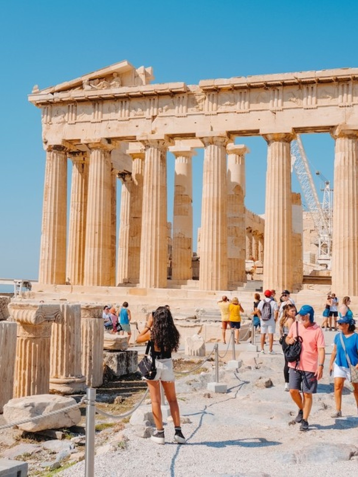 Tourists explore the Parthenon ruins under a clear blue sky.