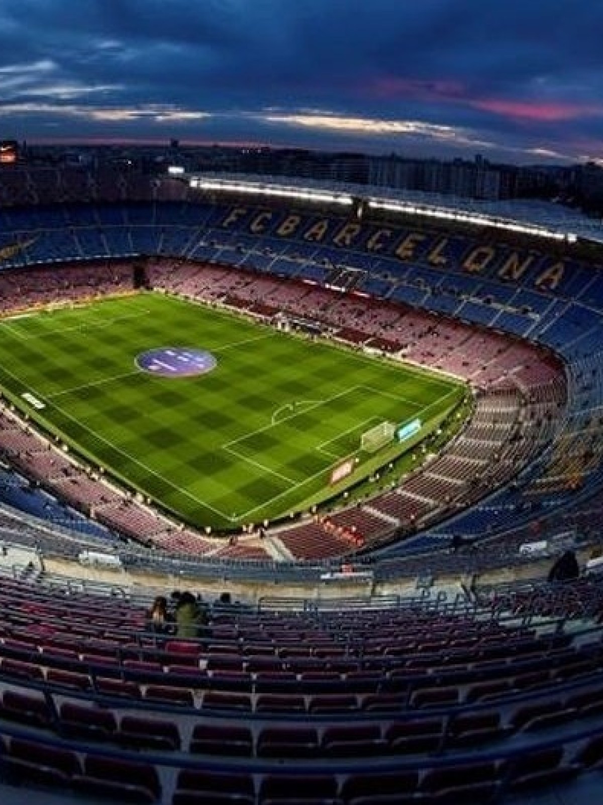 Empty stadium with lit field during sunset, large seating area visible.
