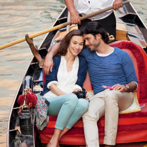 Couple sitting on a gondola, cuddling, with oarsman standing behind them.