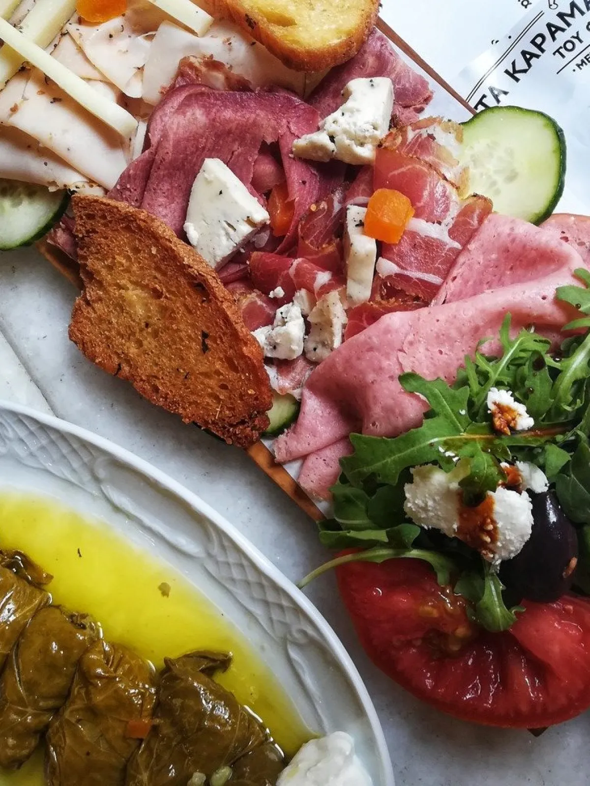 Charcuterie board with meats, cheese, salad, and dolmas on a plate with lemon slice.