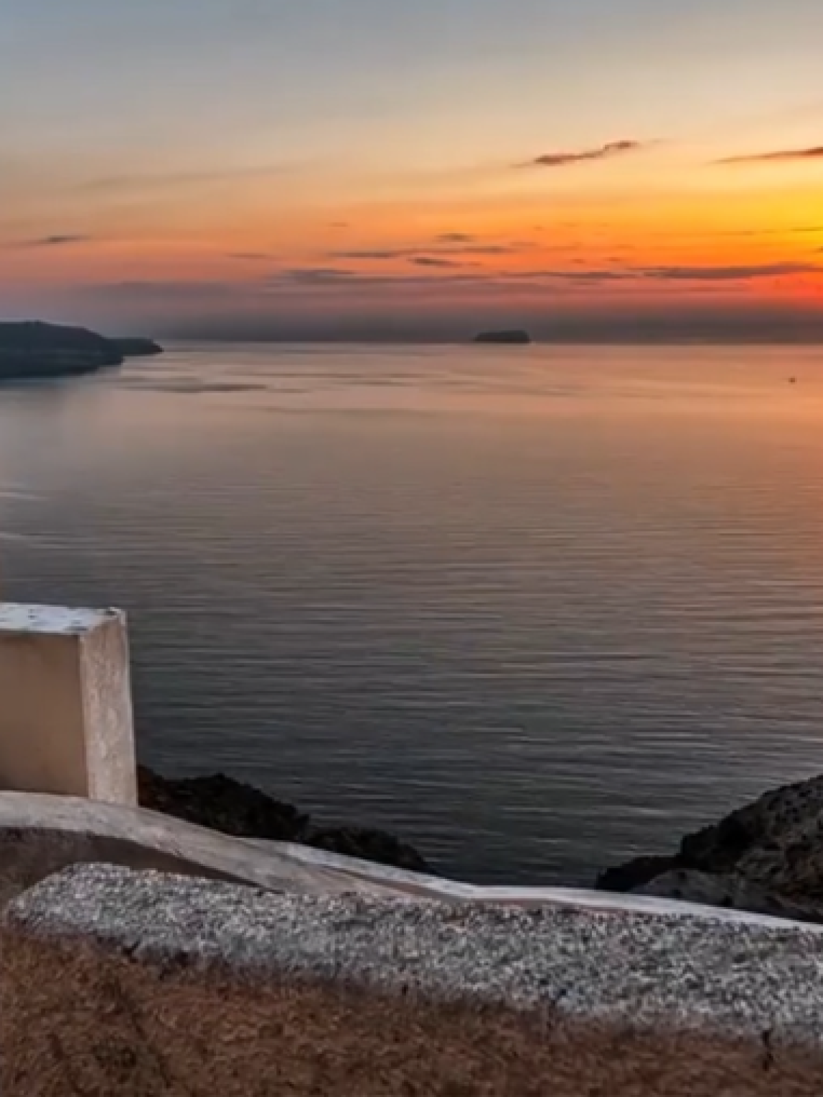 Sunset view over a calm sea with a white church bell tower in the foreground.