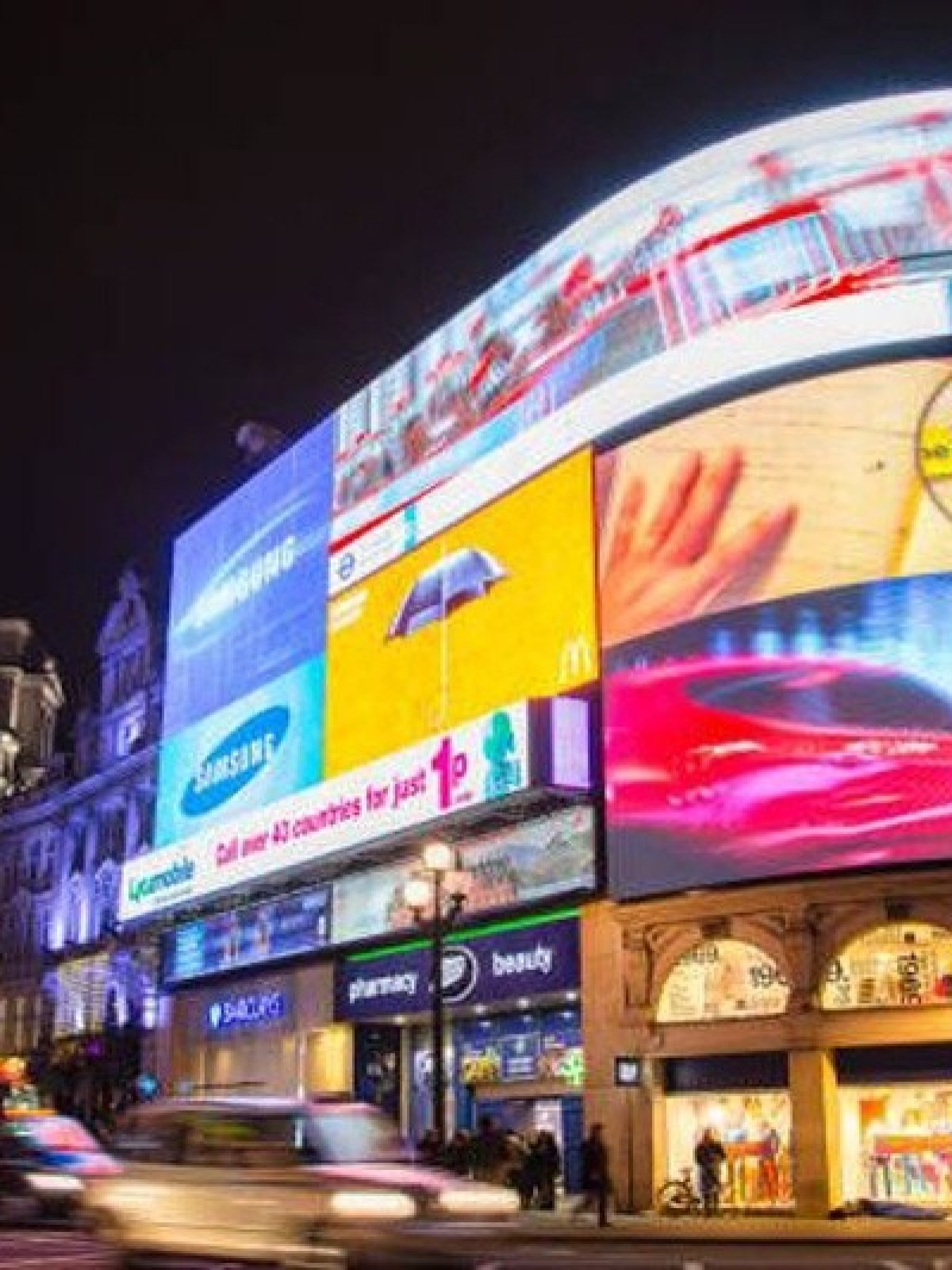 Night scene of busy street with illuminated billboards and a red double-decker bus.