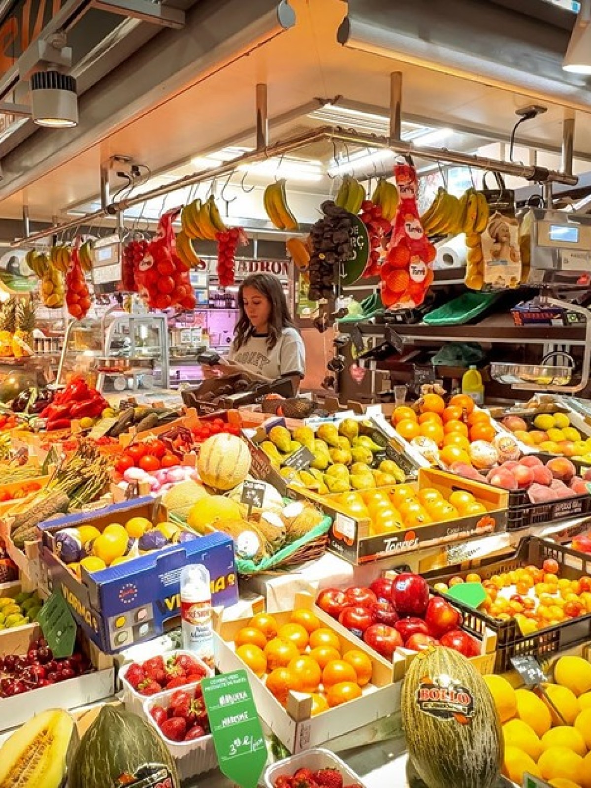 Market stall with a vibrant display of various fruits and two people shopping.