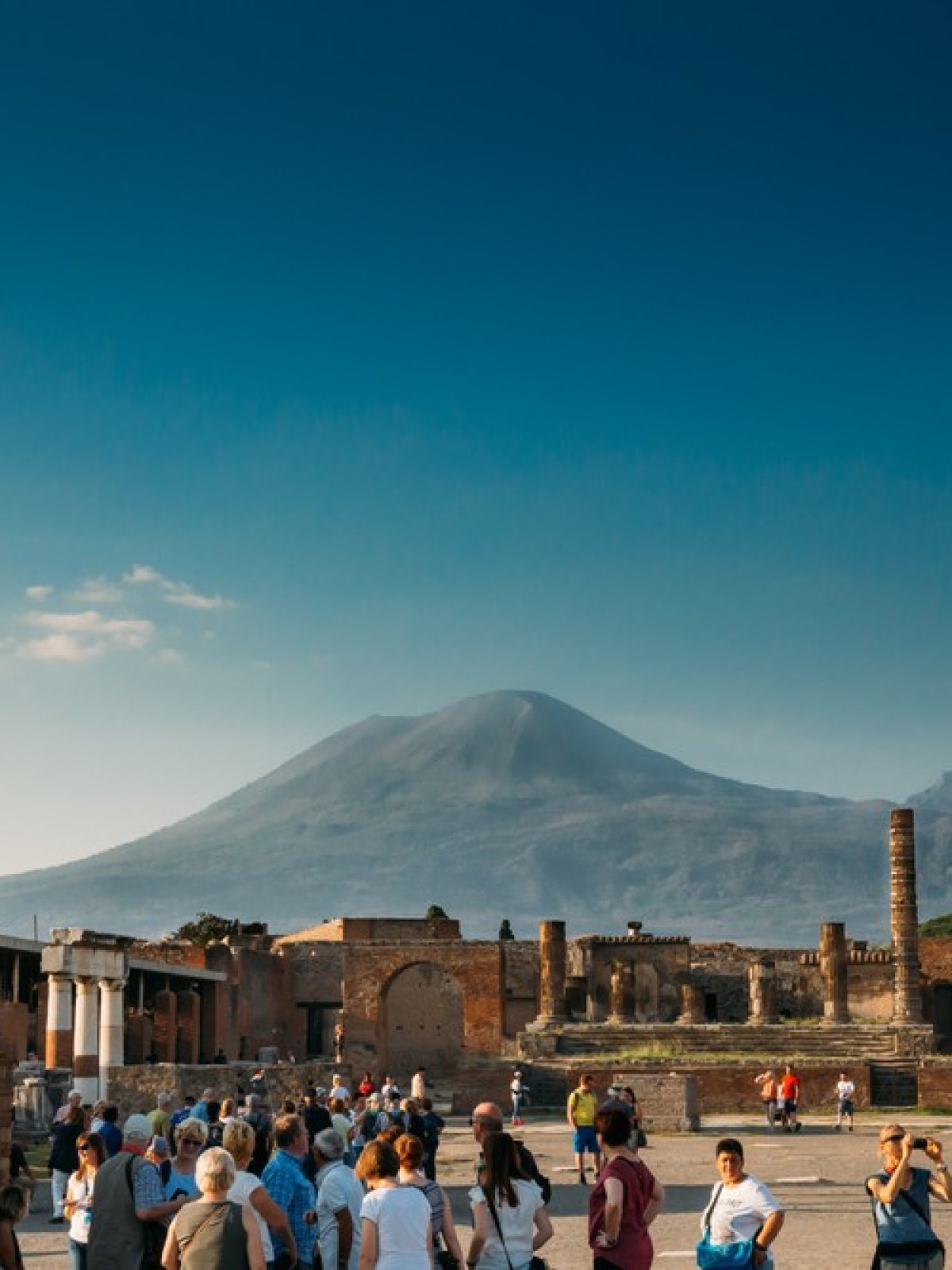 Crowd at Pompeii ruins with Mount Vesuvius in background under a clear blue sky.