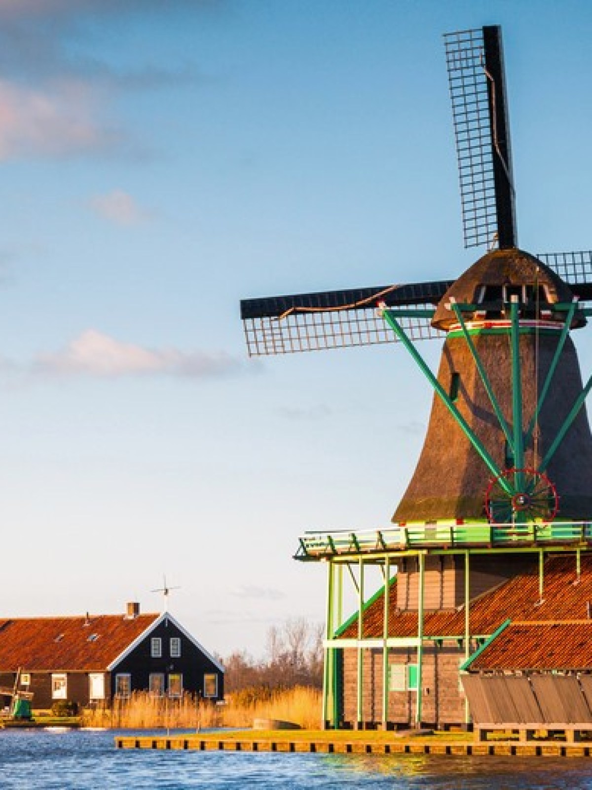 Two traditional windmills by the water under a blue sky.