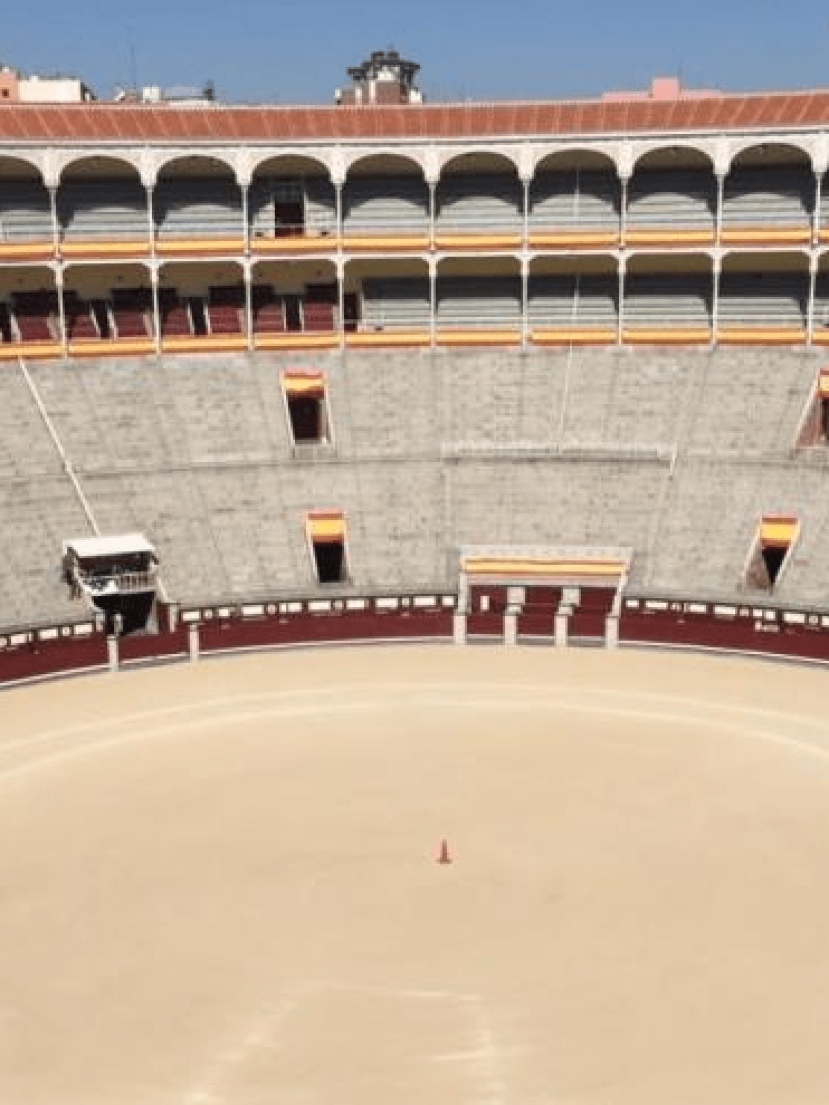 Empty bullring with tiered seating and a cone in the center of the arena.