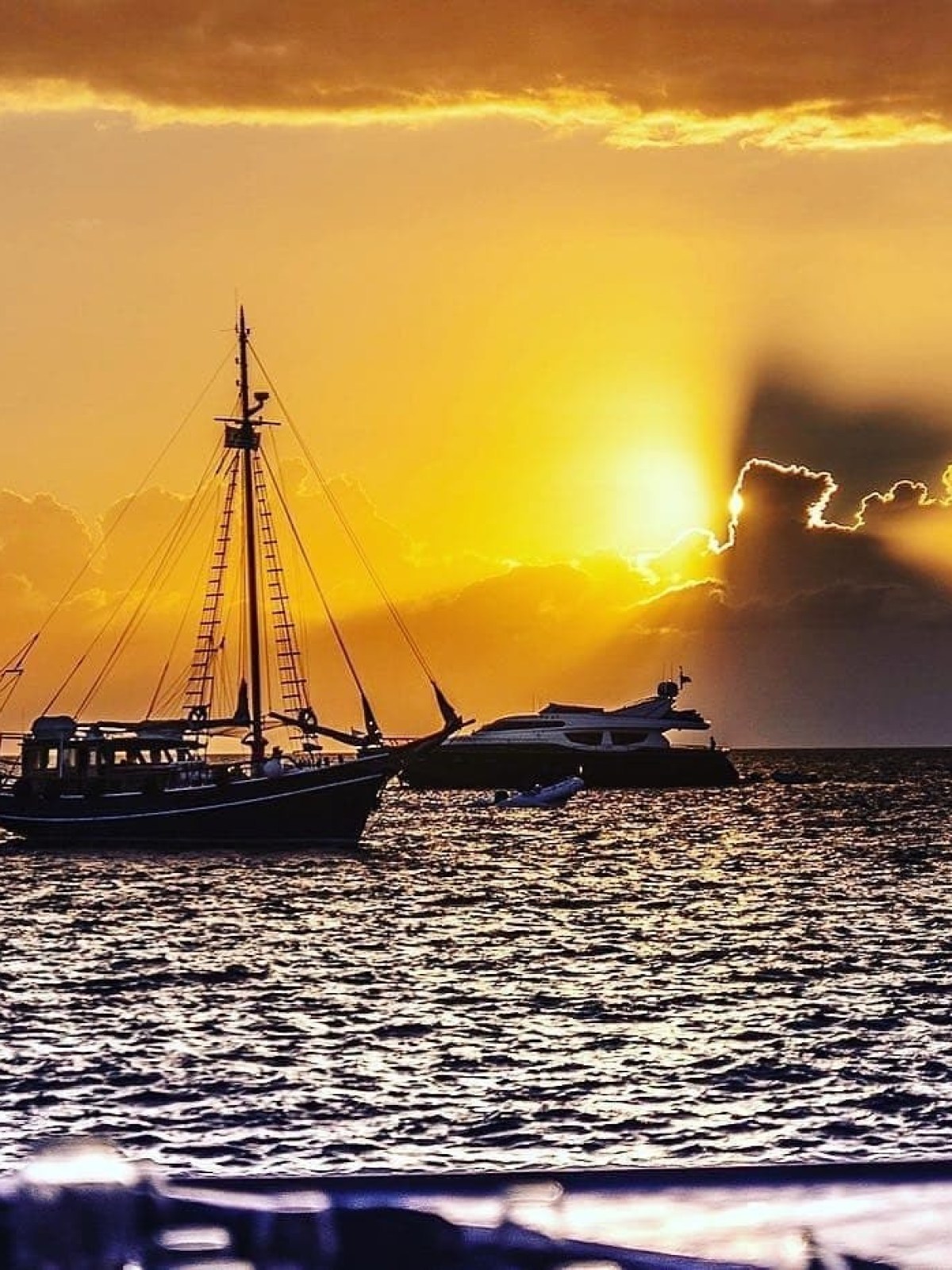 Sailboat and yacht silhouetted against a vibrant sunset over the ocean.