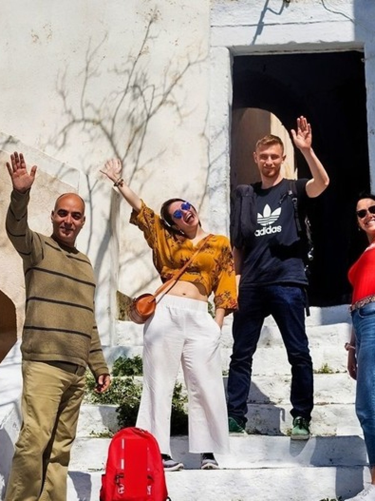 Four people stand on white stairs outdoors, smiling and waving at the camera.