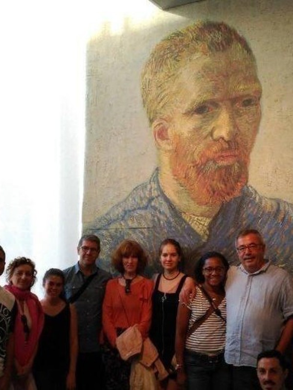 Group of people posing in front of a large mural of a bearded man with red hair.