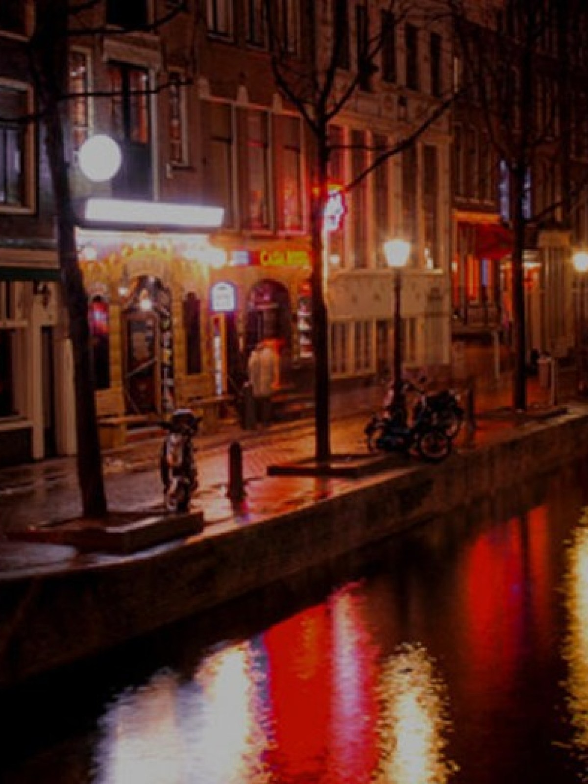 A canal and street in a city at night, lit by colorful lights reflecting on the water.