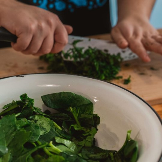Person chopping spinach on a wooden board with a bowl of leaves nearby.