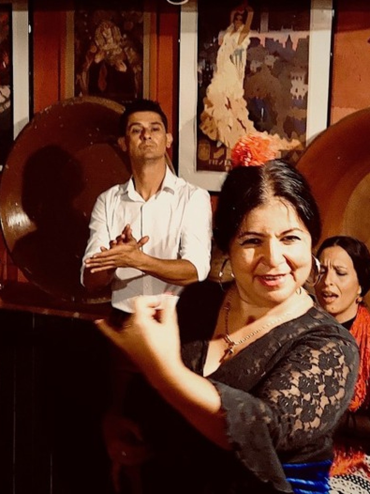 Flamenco dancer in black dress performs live with guitarist and onlookers in a cozy room.