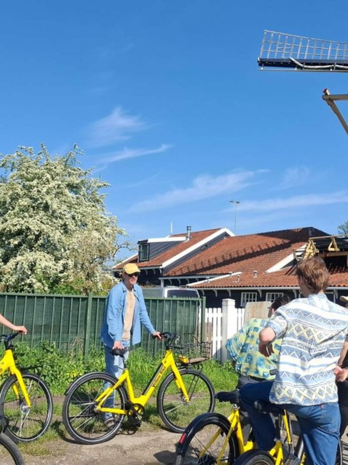 Group of people on yellow bikes in front of a windmill on a sunny day.