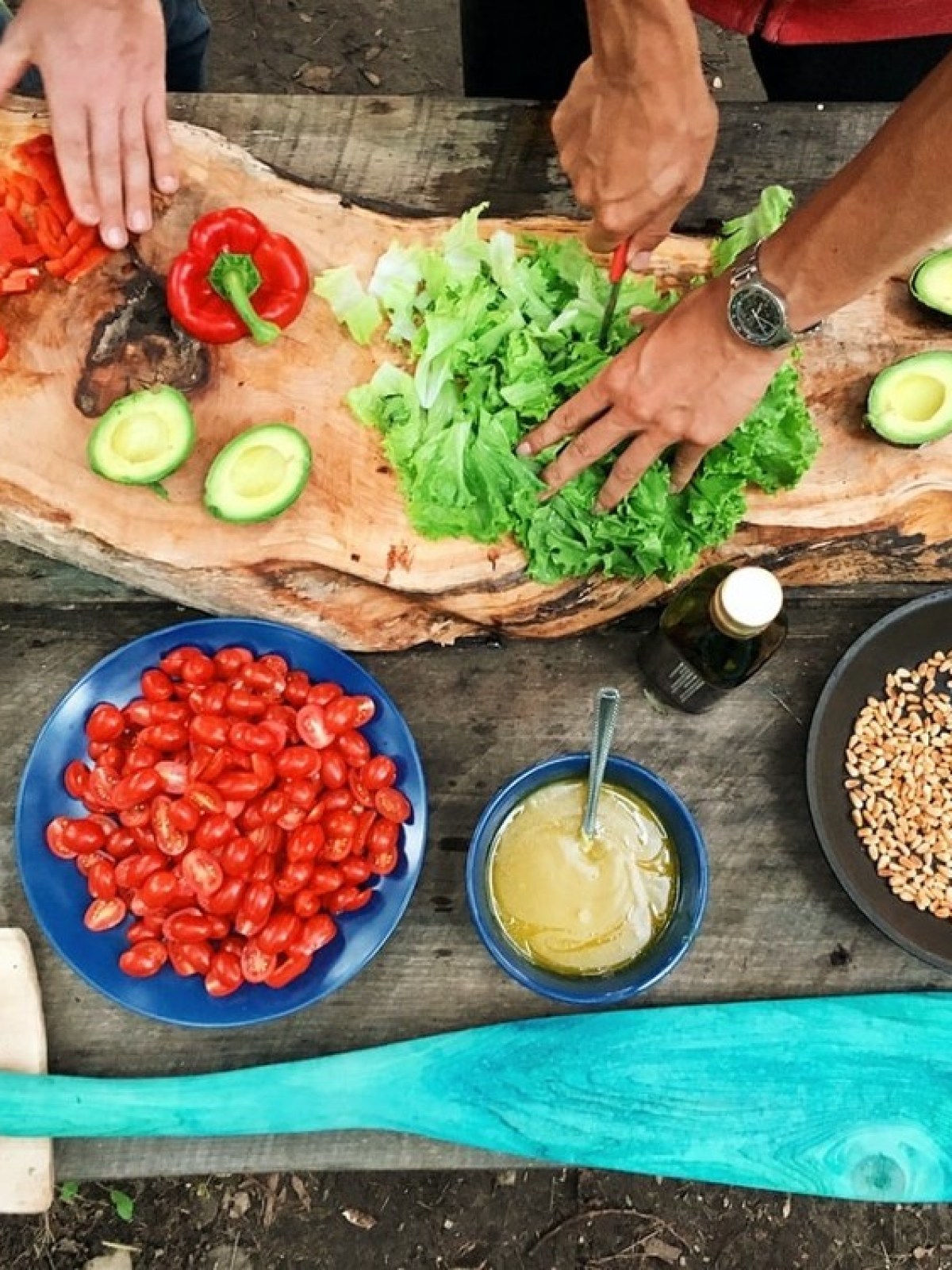 People preparing vegetables on wooden board with bowls of salad ingredients nearby.