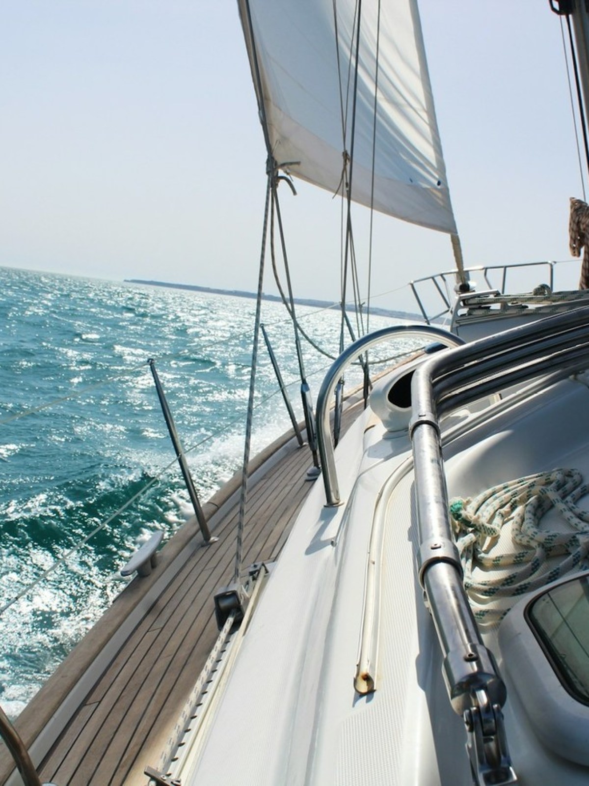 Sailboat on a sunny day with open sails, cruising on blue ocean water.