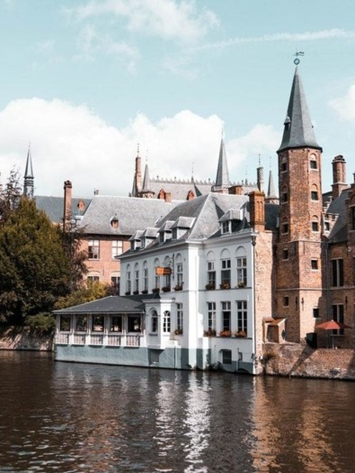 Scenic view of historic buildings by a canal under blue sky in Bruges, Belgium.