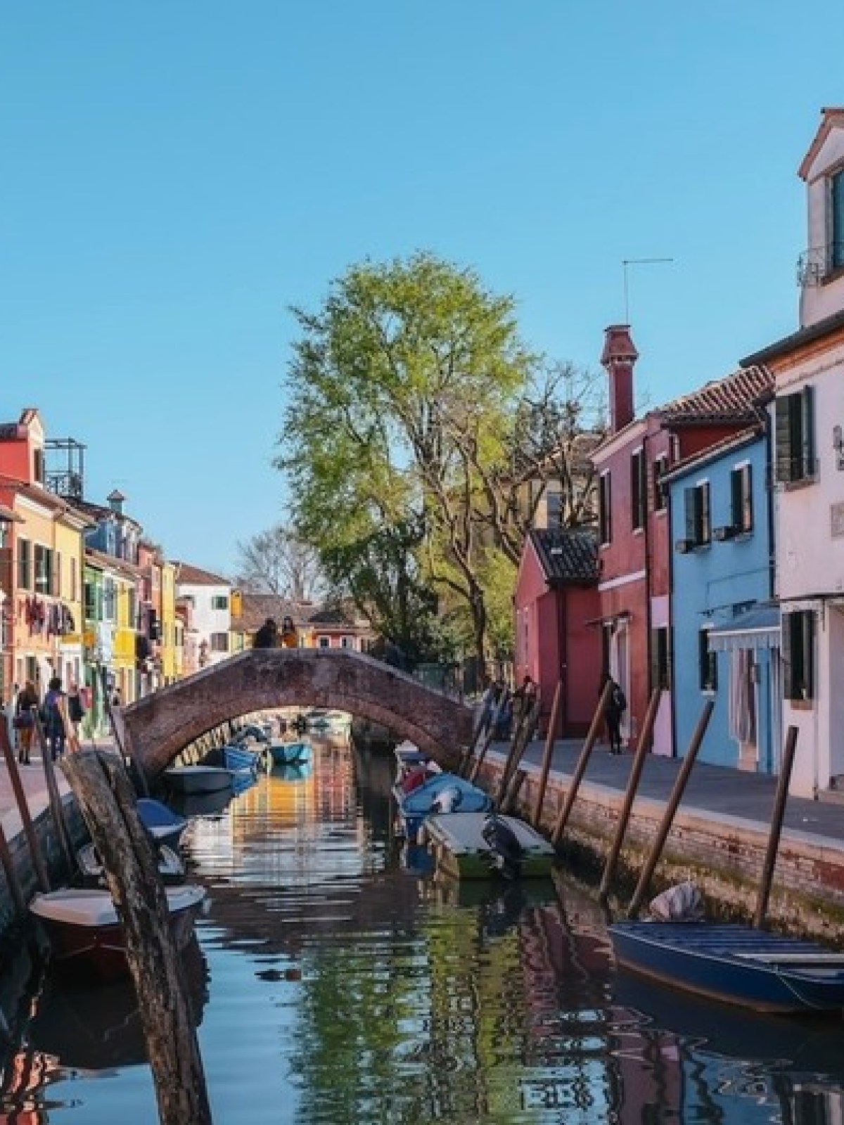 Colorful houses line a canal with boats and a small arched bridge in a quaint neighborhood.