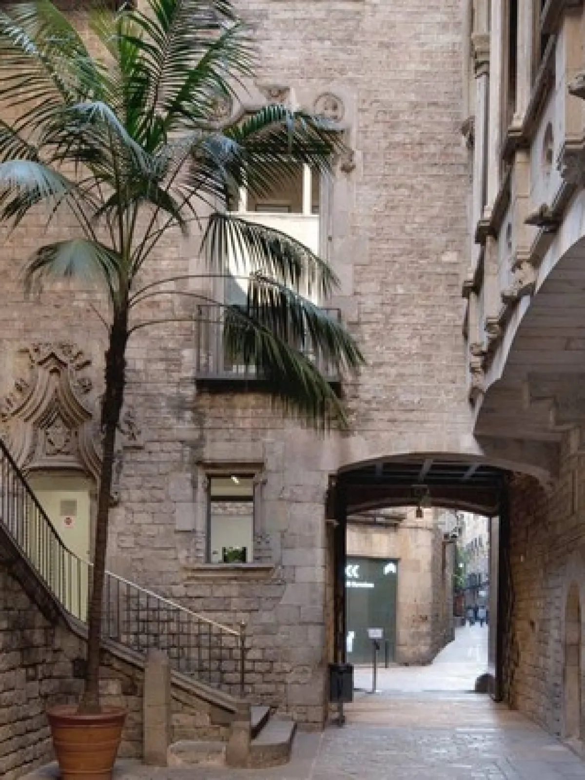 Historic stone alley with potted palm tree, arched walkway, and plaque on wall.