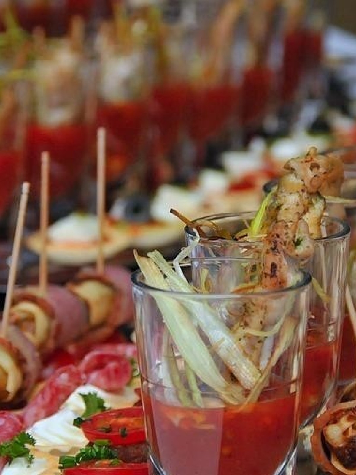 Variety of appetizers and skewers on a platter, with drinks, garnished with herbs and vegetables.
