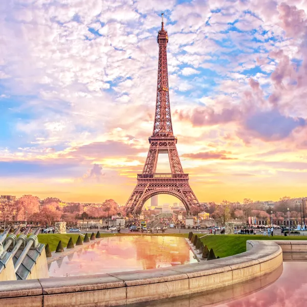 Eiffel Tower at sunset with colorful sky and park view.