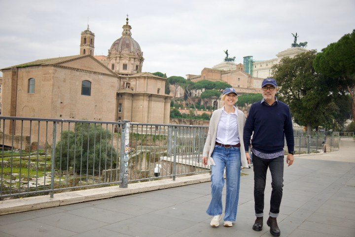 A couple walking by historic buildings in Rome, Italy, on a cloudy day.
